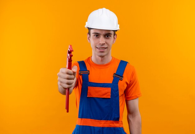 Hombre joven constructor vestido con uniforme de construcción y casco de seguridad sonríe y sostiene alicates de ranura