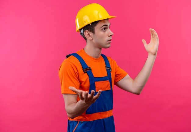 Hombre joven constructor vestido con uniforme de construcción y casco de seguridad sorprendido