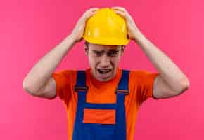 Foto gratuita hombre joven constructor vestido con uniforme de construcción y casco de seguridad sosteniendo su cabeza con las manos