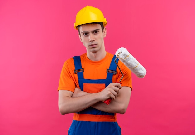 Hombre joven constructor vestido con uniforme de construcción y casco de seguridad sostiene un cepillo de rodillo