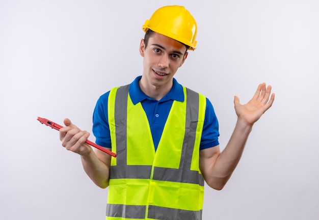 Hombre joven constructor vestido con uniforme de construcción y casco de seguridad tiene unos alicates de ranura