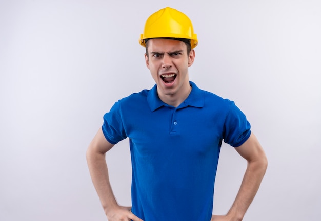 Hombre joven constructor vestido con uniforme de construcción y gritos de casco de seguridad