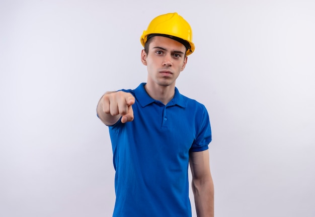 Hombre joven constructor vestido con uniforme de construcción y puntos de casco de seguridad con el dedo índice