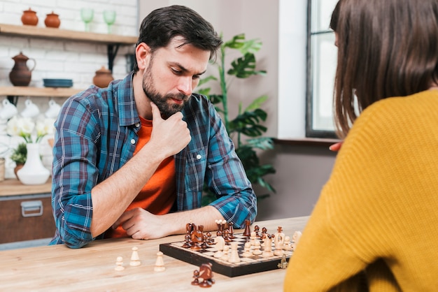 Hombre joven contemplado que juega el juego de ajedrez con su esposa en casa