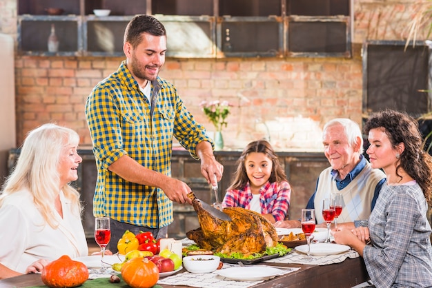 Hombre joven cortando pollo al horno en la mesa con la familia