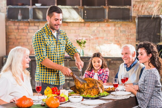 Hombre joven cortando pollo al horno en la mesa con la familia