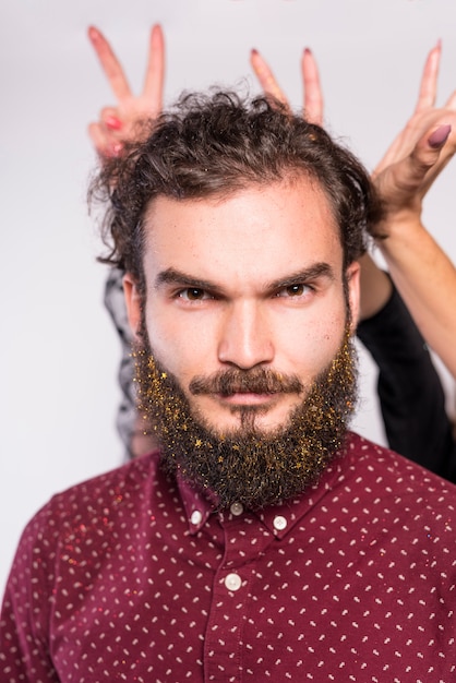 Hombre joven con cuernos de dedos detrás de la cabeza.