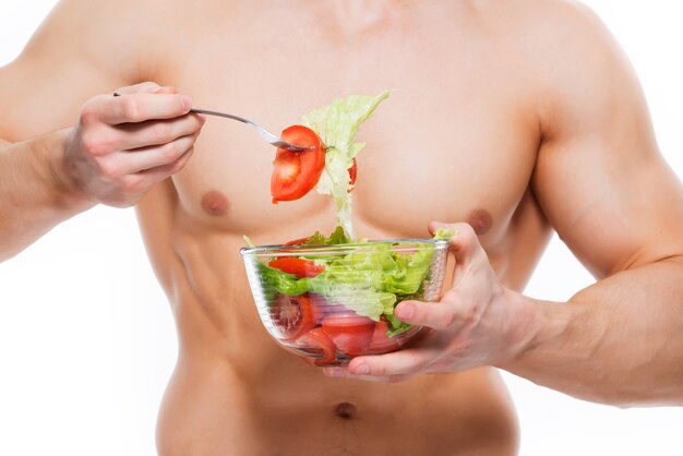 Hombre joven con cuerpo perfecto tiene ensalada - aislada en la pared blanca.