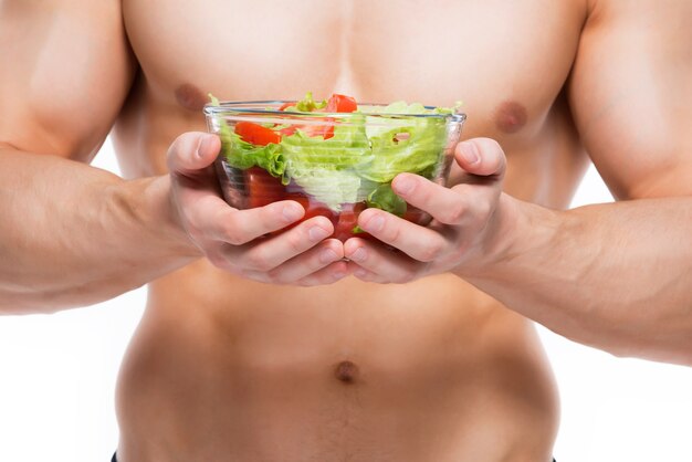 Hombre joven con cuerpo perfecto tiene ensalada - aislada en la pared blanca.