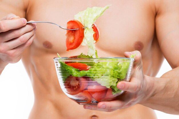 Hombre joven con cuerpo perfecto tiene ensalada - aislada en la pared blanca.