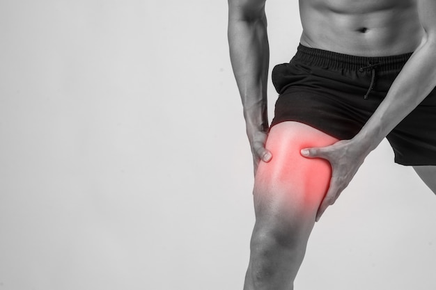 Hombre joven del deporte con las piernas atléticas fuertes que sostienen la rodilla con sus manos en dolor después de sufrir lesión del ligamento aislada en blanco.