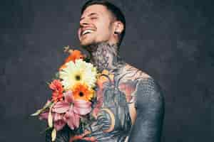 Foto gratuita hombre joven descamisado alegre con orejas perforadas con decoración de flores en su cuerpo tatuado