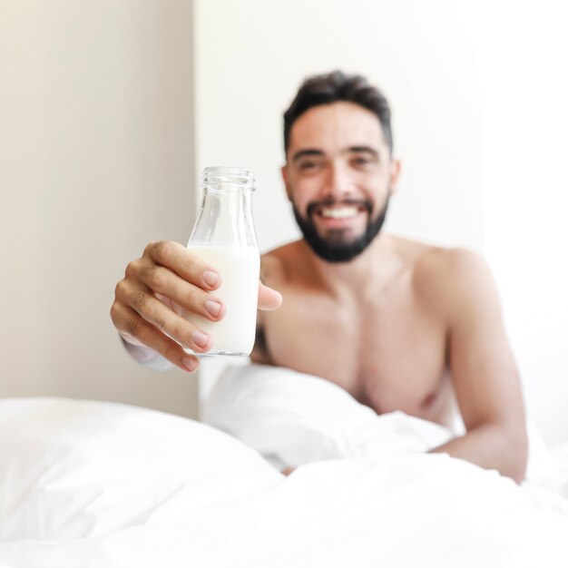 Hombre joven descamisado que sostiene la botella de leche