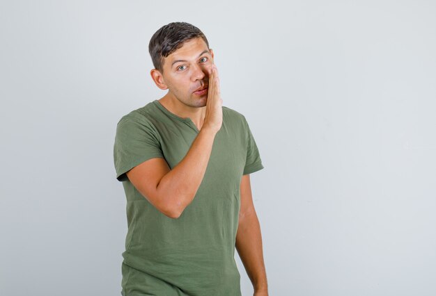 Hombre joven diciendo algo confidencial en camiseta verde militar, vista frontal.