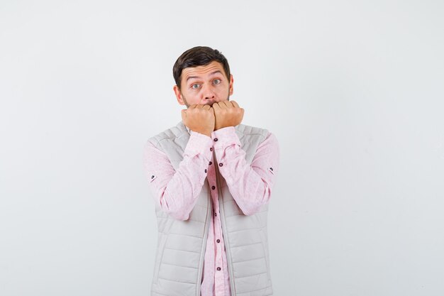 Hombre joven elegante en camisa, chaleco mordiendo los puños emocionalmente y mirando asustado,