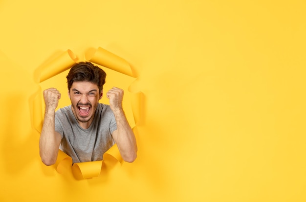 Hombre joven emocionado mirando desde el fondo de papel amarillo rasgado chico interior facial