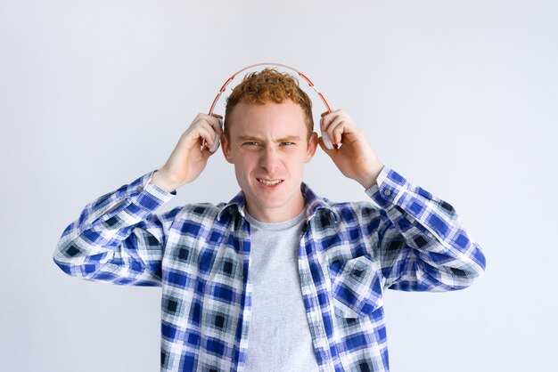 El hombre joven emocionado que sostiene los auriculares acerca a los oídos