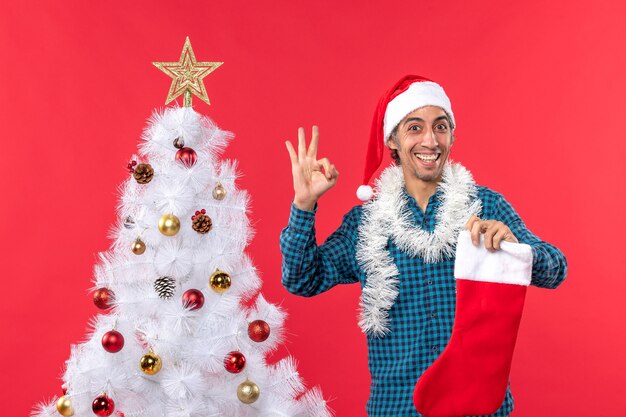 Hombre joven emocionado con sombrero de santa claus en una camisa azul a rayas y sosteniendo un calcetín de navidad