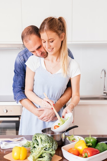 Hombre joven encantador que ama a su esposa que prepara la comida en la cocina