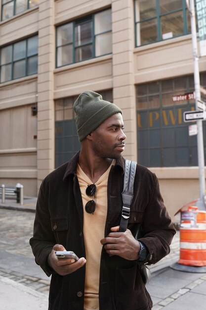 Hombre joven con estilo explorando la ciudad mientras usa un teléfono inteligente