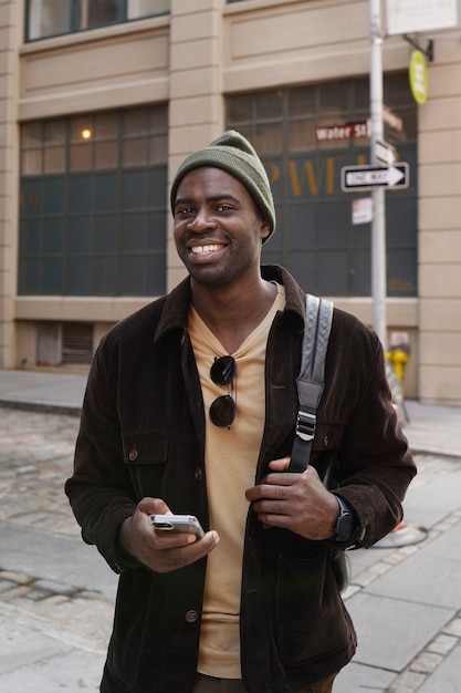 Hombre joven con estilo explorando la ciudad mientras usa un teléfono inteligente