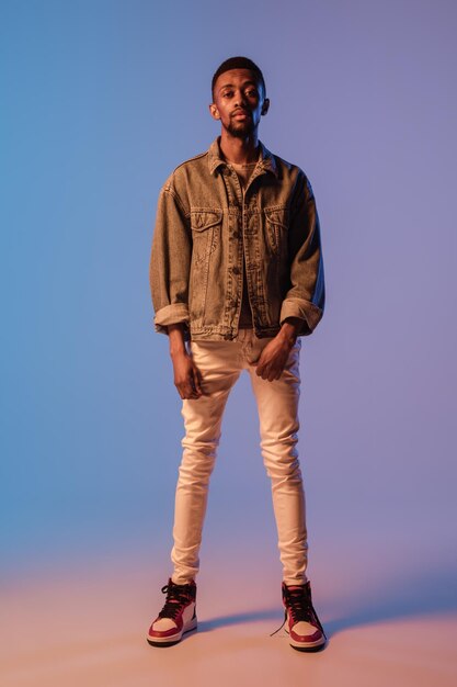 Hombre joven con estilo en traje de estilo callejero moderno aislado sobre fondo degradado en luz de neón Modelo de moda afroamericano en look book músico interpretando