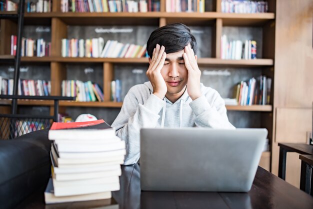 Hombre joven estudiante cansado de la computadora sentado en la mesa de café con la computadora portátil