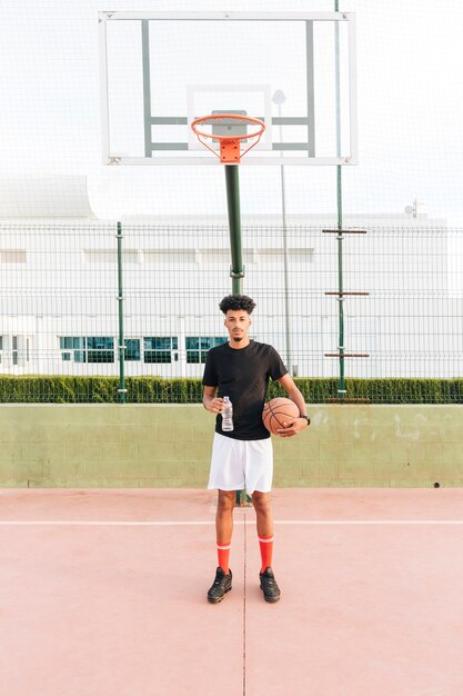 Hombre joven étnico que sostiene baloncesto en la corte