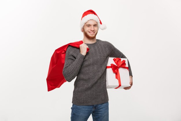 Hombre joven feliz de la barba que sostiene el bolso de santa y el presente blanco.