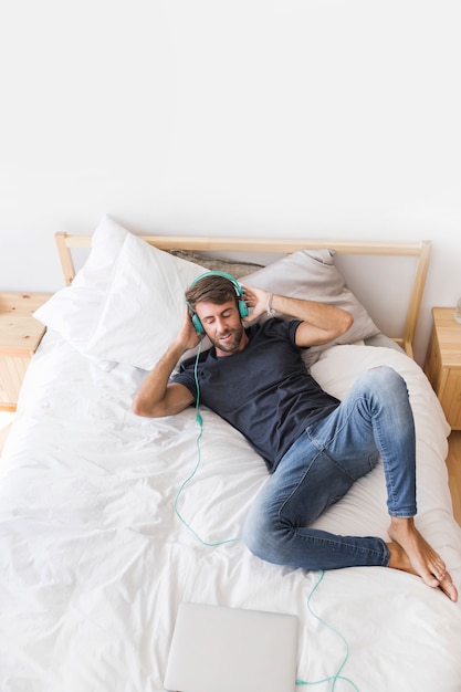 Hombre joven feliz escuchando música en la cama