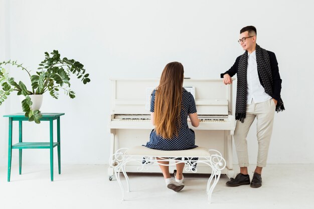 Hombre joven feliz con la mano en su bolsillo mirando a la mujer tocando el piano