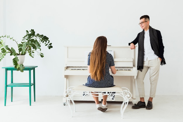 Hombre joven feliz con la mano en su bolsillo mirando a la mujer tocando el piano