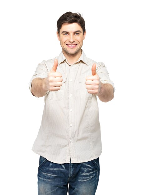 Hombre joven feliz con pulgares arriba firmar en casuals aislado en la pared blanca.