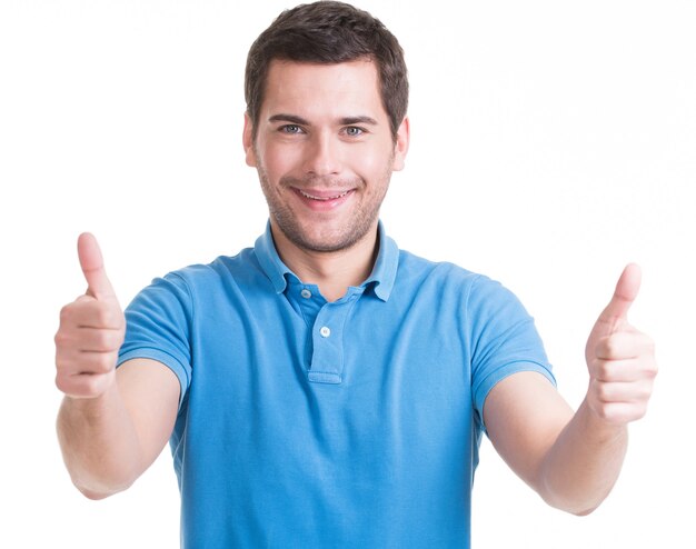 Hombre joven feliz con pulgares arriba firmar en casuals aislado en la pared blanca.