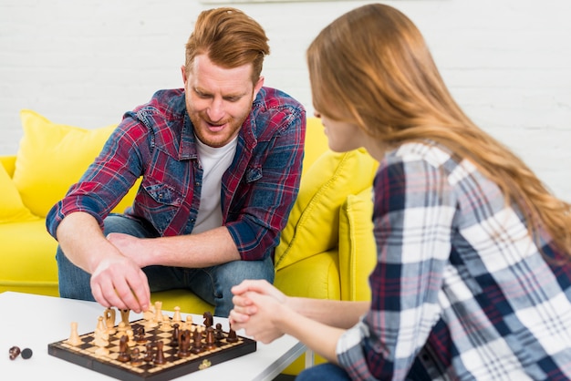 Hombre joven feliz que juega al ajedrez con su novia en casa