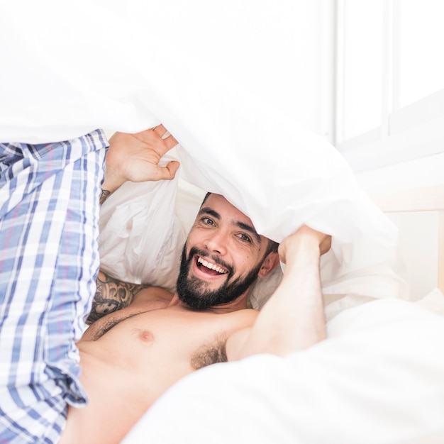 Hombre joven feliz que mira debajo de la manta