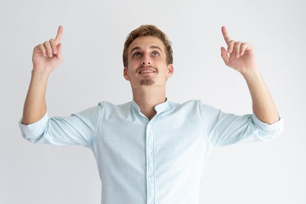 Hombre joven feliz que señala y que mira hacia arriba