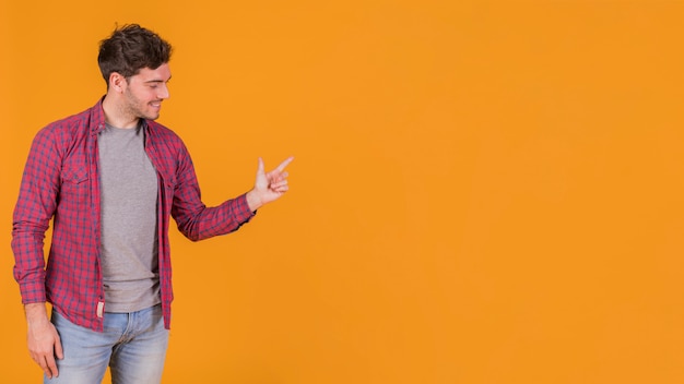 Hombre joven feliz que señala su dedo contra un fondo naranja