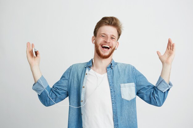 Hombre joven feliz que sonríe escuchando la transmisión de música en auriculares que canta.