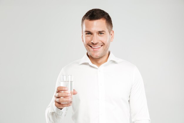Hombre joven feliz que sostiene el vaso lleno de agua.