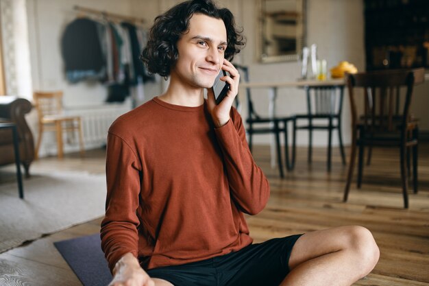 Hombre joven feliz en ropa casual que pasa todo el día en casa solo mientras el distanciamiento social, sonriendo