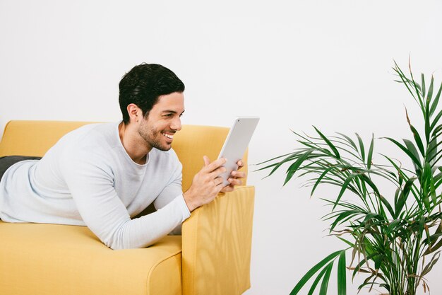 Hombre joven feliz tumbado en el sofá con la tablet