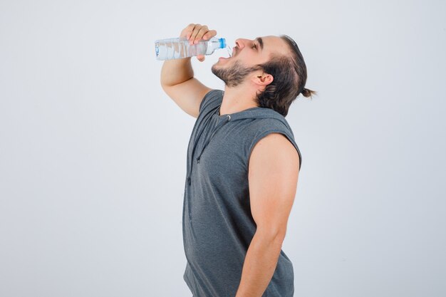 Hombre joven en forma en agua potable con capucha sin mangas y mirando alegre, vista frontal.