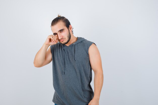 Hombre joven en forma frotándose el ojo con chaleco sin mangas y mirando molesto, vista frontal.