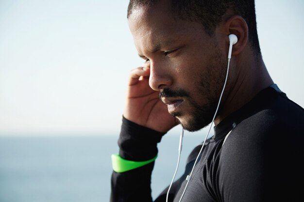 Hombre joven en forma en la playa escuchando música