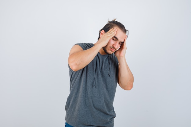 Hombre joven en forma con sudadera con capucha sin mangas que sufre de dolor de cabeza y se ve mal, vista frontal.