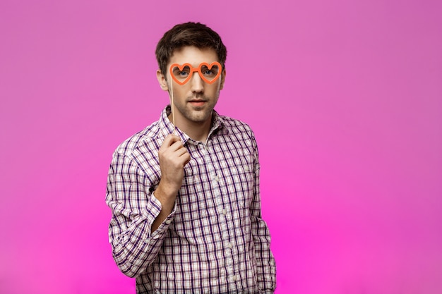 Hombre joven con gafas falsas sobre pared púrpura. Fiesta de cumpleaños.