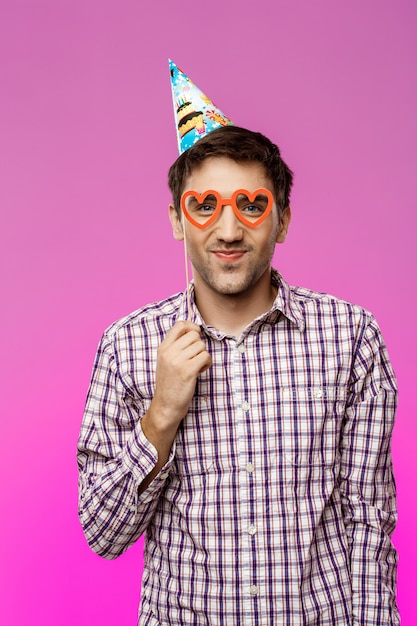 Hombre joven con gafas falsas sobre pared púrpura. Fiesta de cumpleaños.