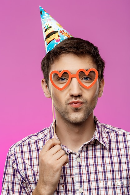 Hombre joven con gafas falsas sobre pared púrpura. Fiesta de cumpleaños.