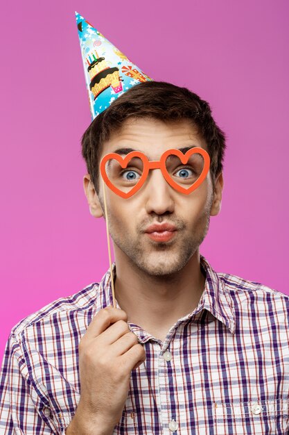 Hombre joven con gafas falsas sobre pared púrpura. Fiesta de cumpleaños.